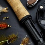 detailed view of fly fishing gear including rod reel and colorful flies on a dark surface